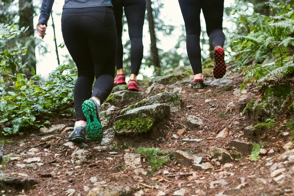 Three runners run up a hill in the woods. 