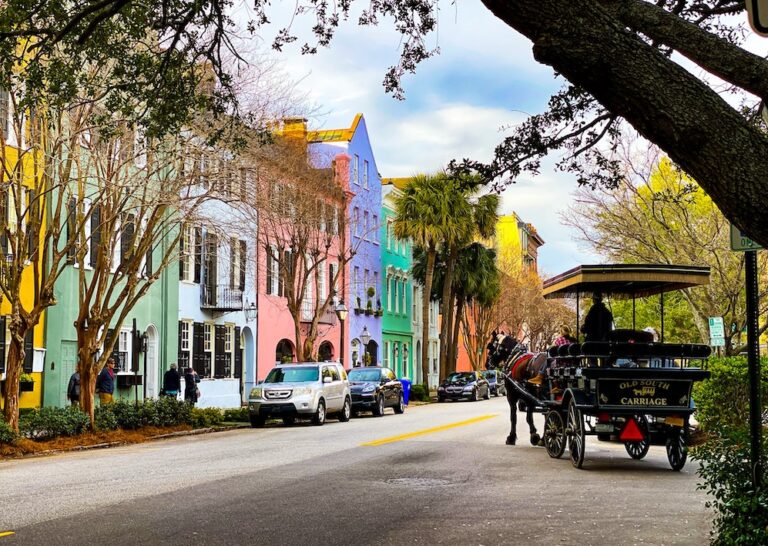 A horse-drawn carriage drives tourists past a row of rainbow colored houses in Charleston, South Carolina.
