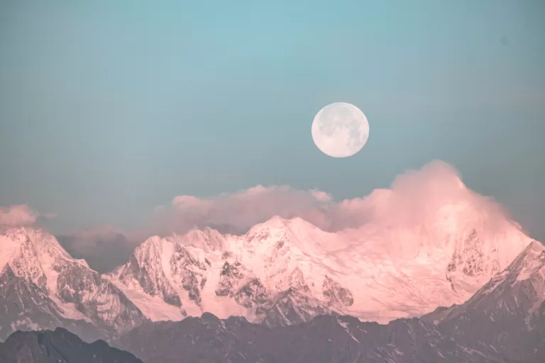 A full moon rising above the mountains.