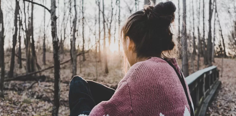 Dark-haired woman in a pink sweater staring into the woods.