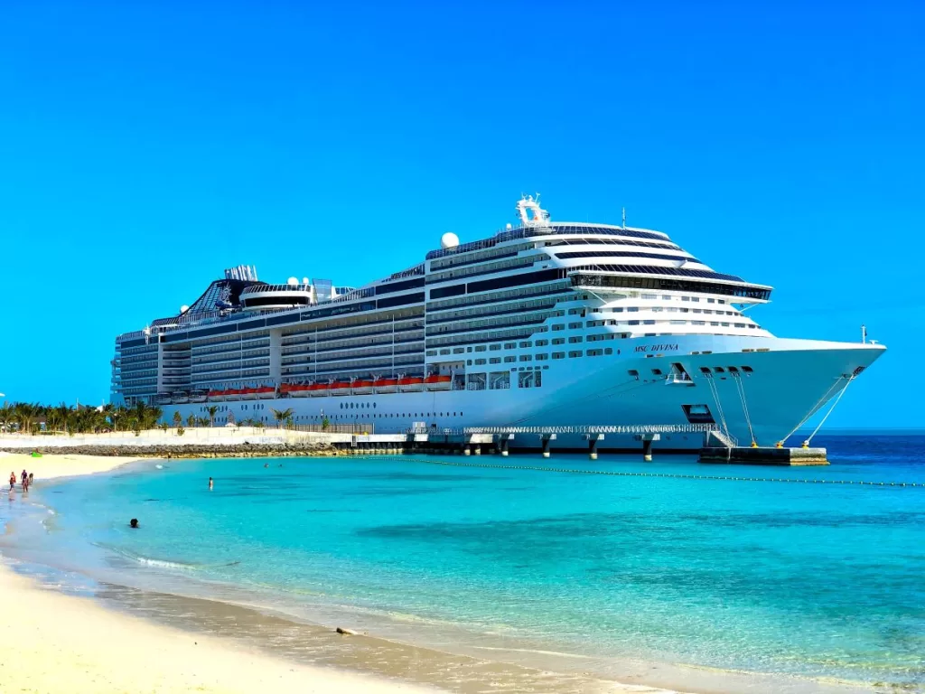 A cruise ship at port with vibrant blue sky in the background and blue-green calm ocean with a light colored sandy beach.