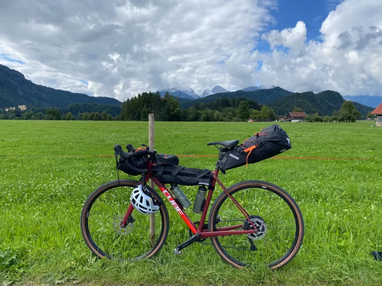 A bicycle with loaded panniers in a field with mountains in the background