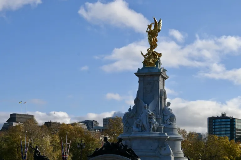 A gold plated statue in a city square, with a bright blue sky and some clouds.