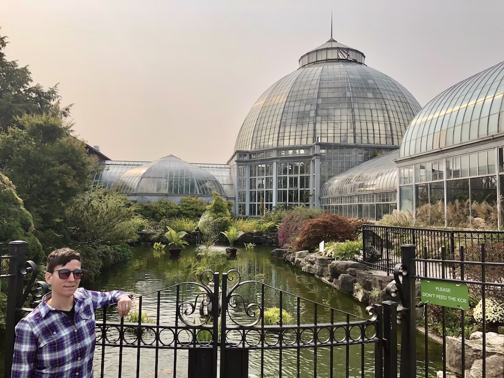 The author in plaid shirt standing in front of conservatory glasshouse. 