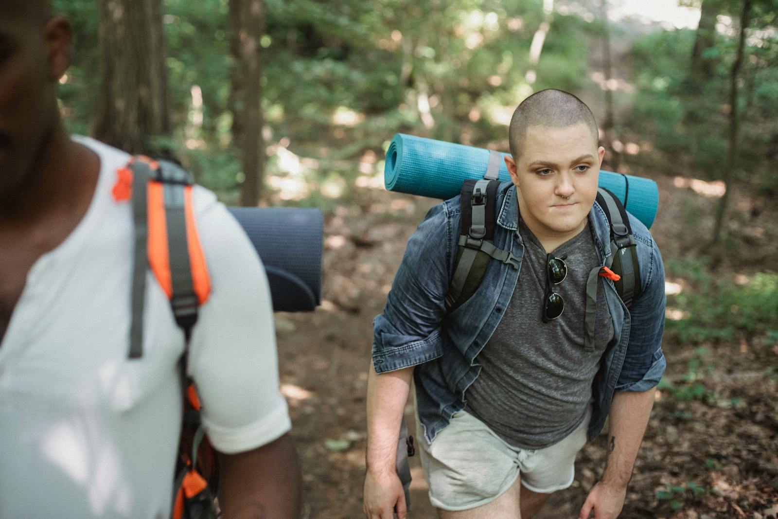 Trans man hiking with backpack in a bright summer forest.