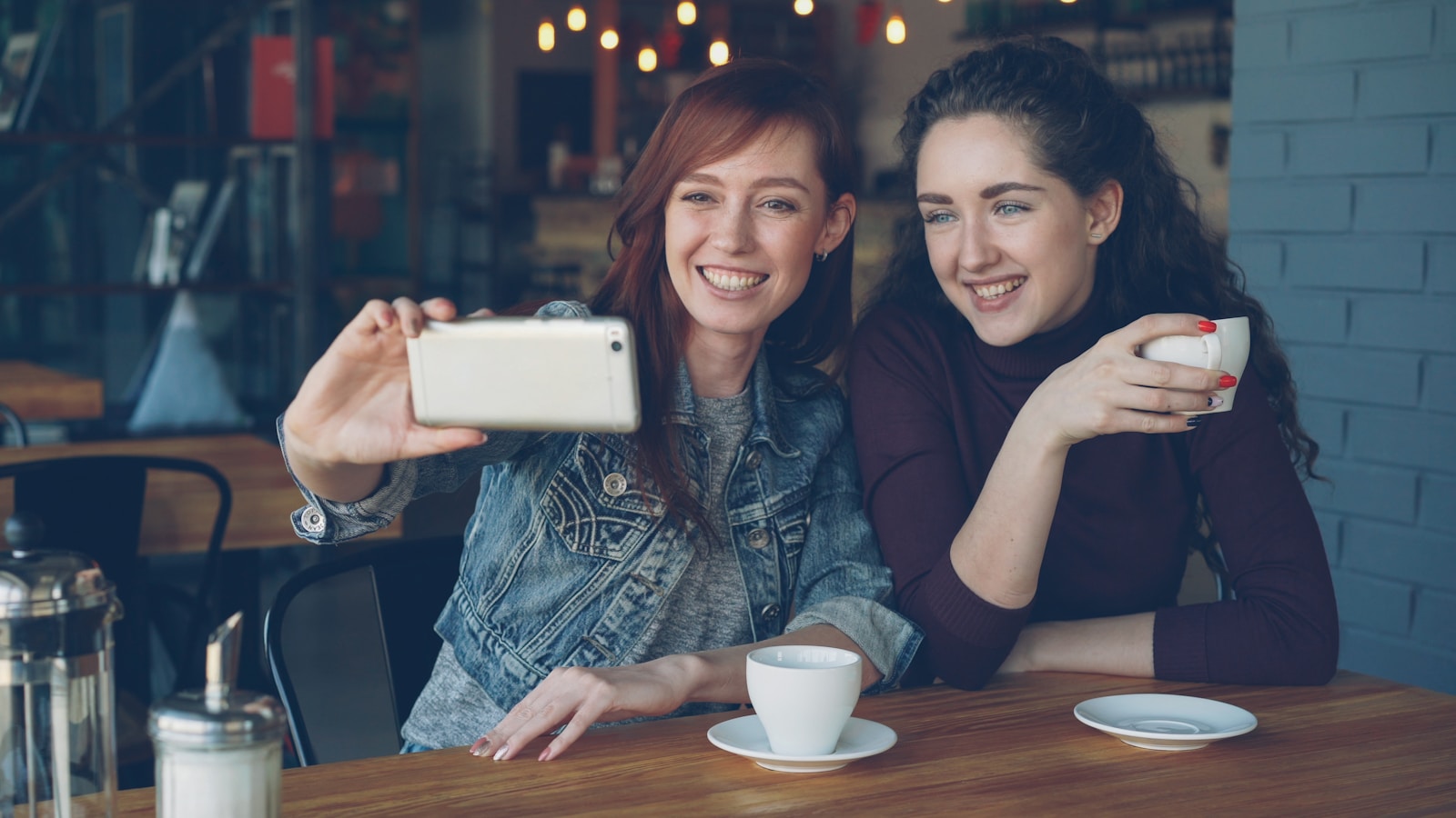 Two friends take a selfie in a cafe.