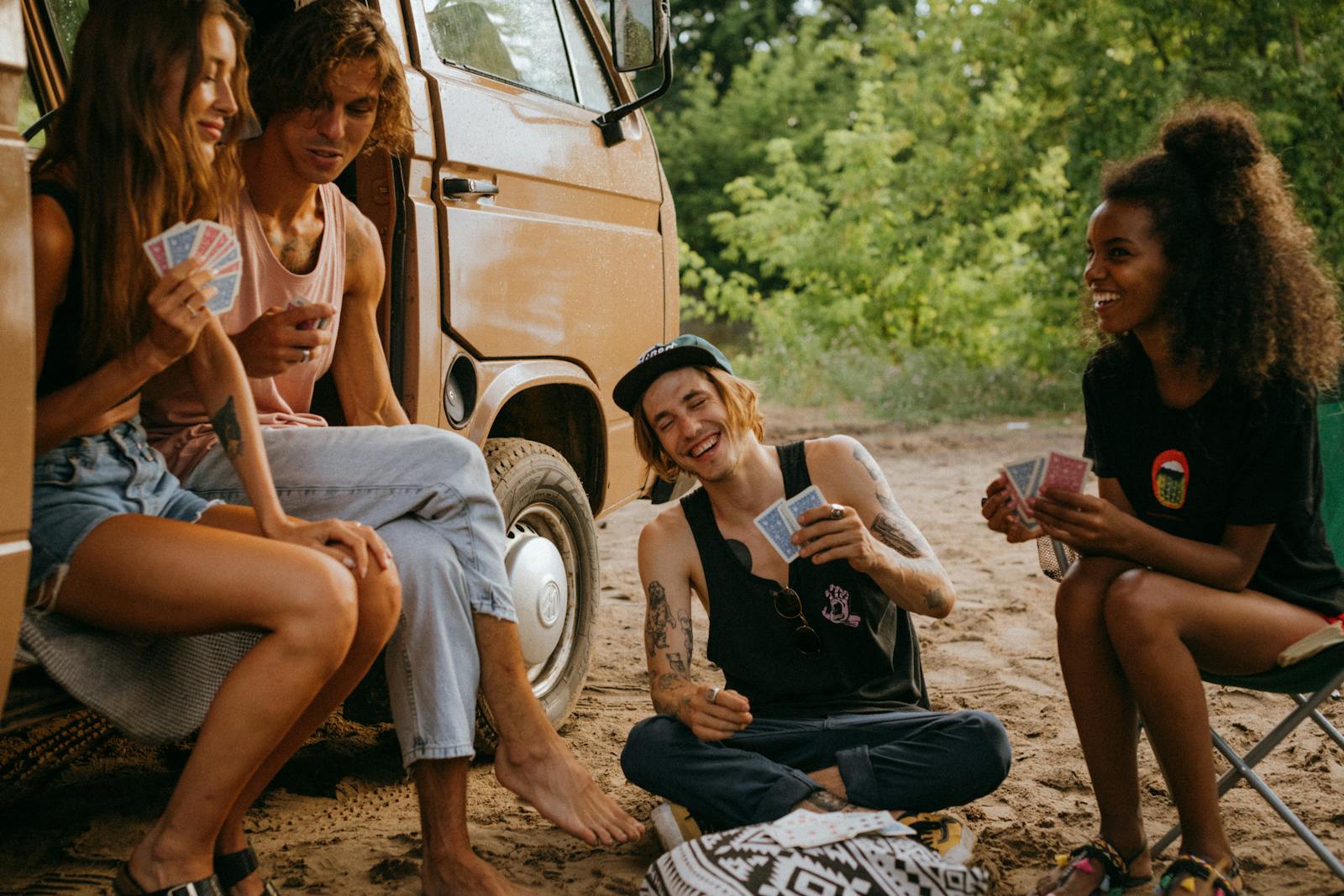 Group of friends playing cards by a camper van in a sunny outdoor setting.